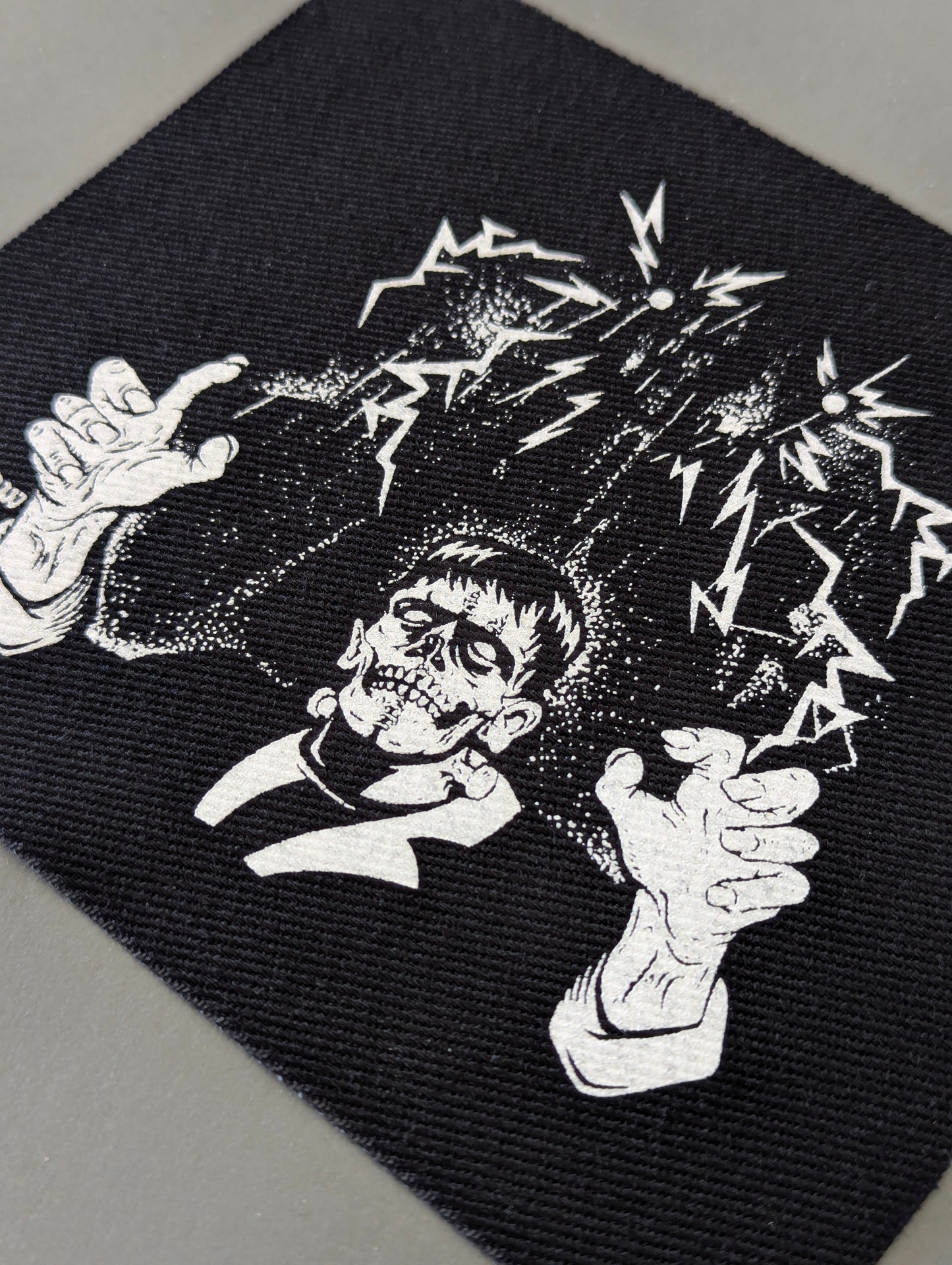 Black fabric patch with a skeleton design and electric sparks on a black background