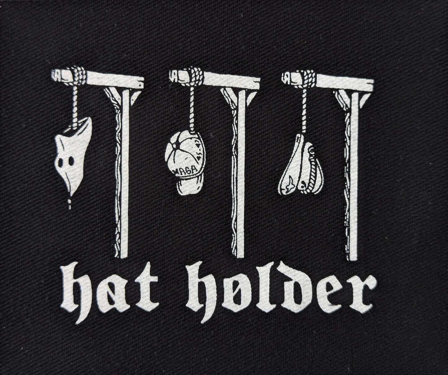 Black patch with white text and illustrations of hats on hooks, labeled 'hat holder'.