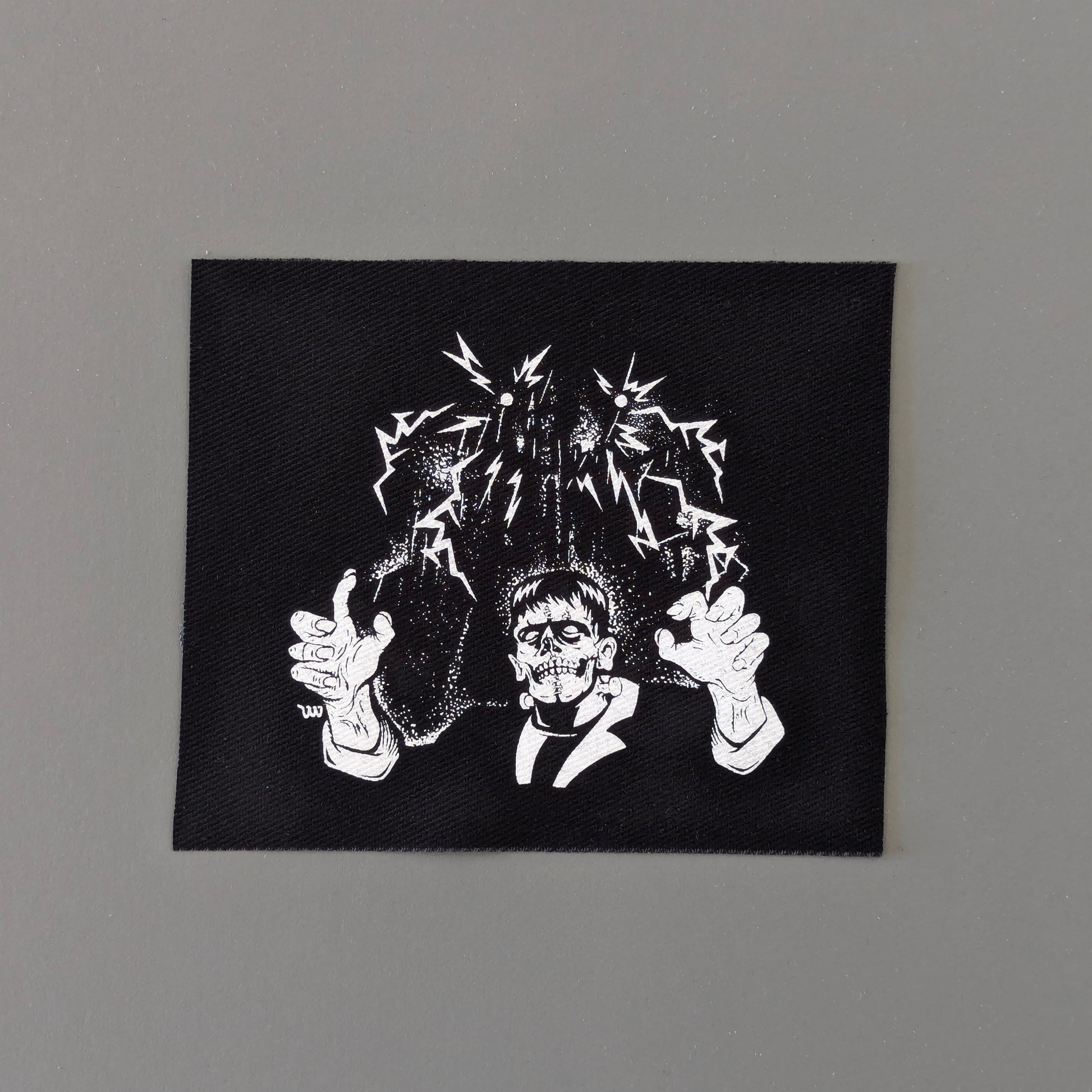 Black square patch with white graphic design on a gray background