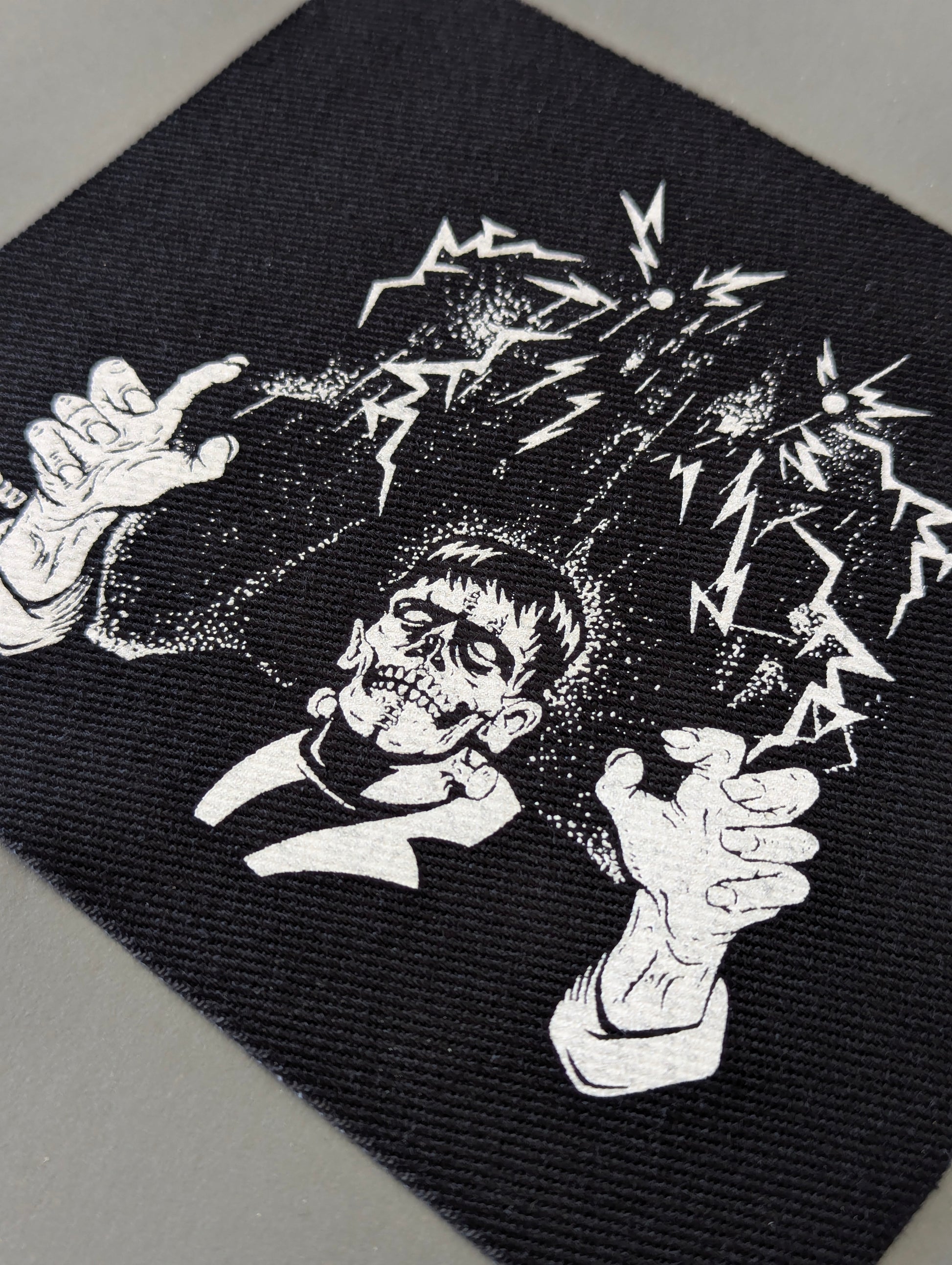 Black fabric patch with a skeleton design and electric sparks on a black background